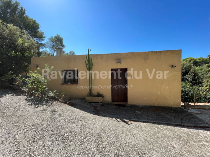 Maison jaune avec porte en bois et fenêtre grillagée.
